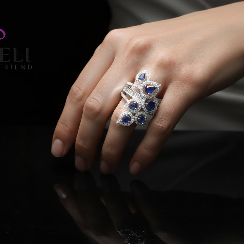 Elegant ring with blue gemstones and diamonds on a gray background, featuring the brand 'Saheli'.