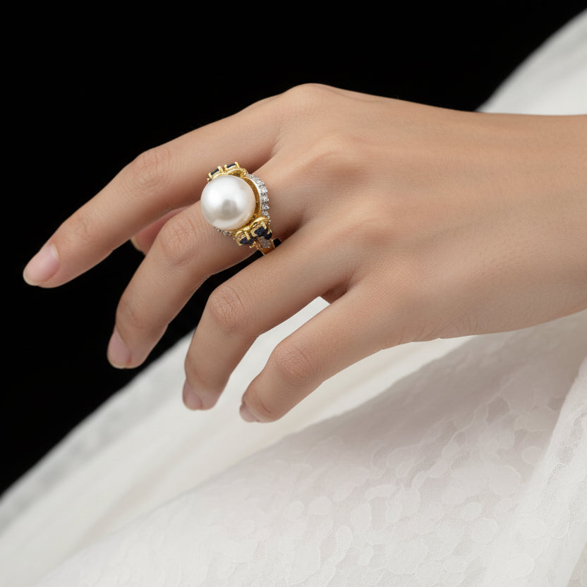 Gold ring with a pearl on a dark background, featuring the brand 'Saheli'.