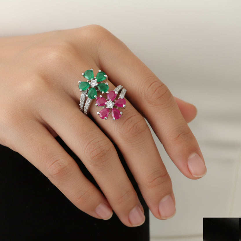 Decorative ring with green and pink gemstones on a black hand, branded 'SAHELI'.