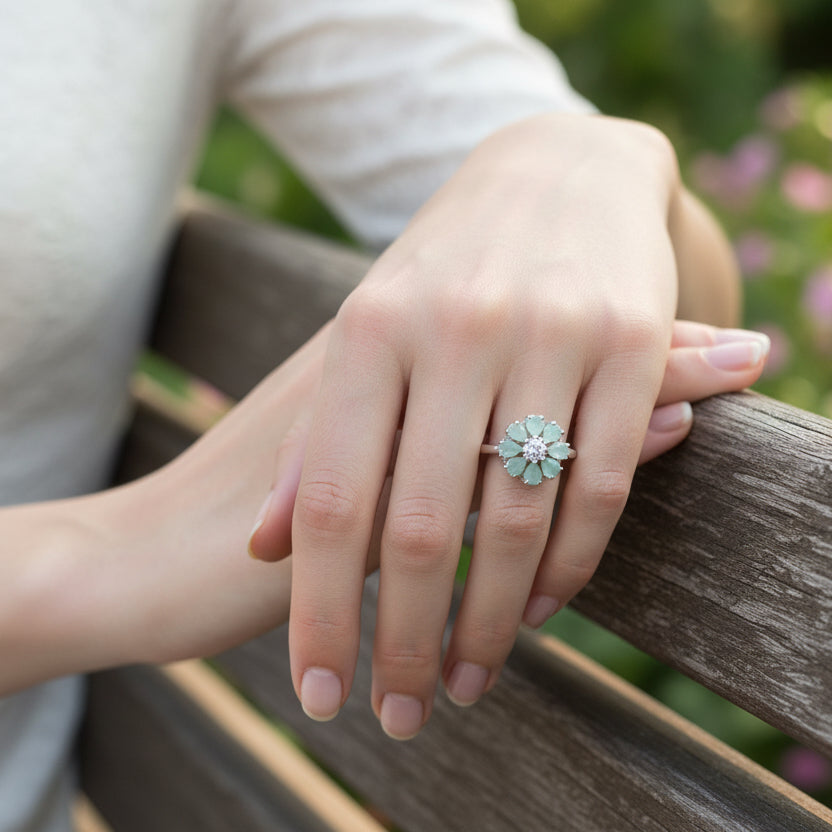 Floral silver ring with green gemstones on a black gloved hand against a dark background