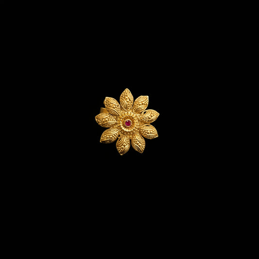 A gold flower-shaped ring with a small red gemstone in the center, displayed on a dark reflective surface. The brand logo 'SAHELI MY BEST FRIEND' is visible in the top left corner.
