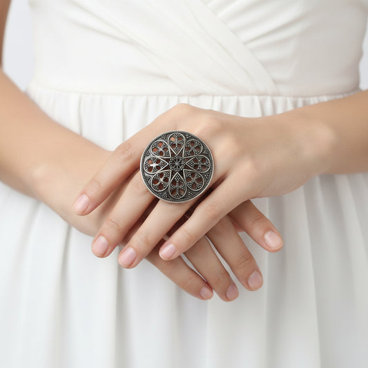 Decorative ring with intricate design on a black mannequin hand, branded 'Saheli'.