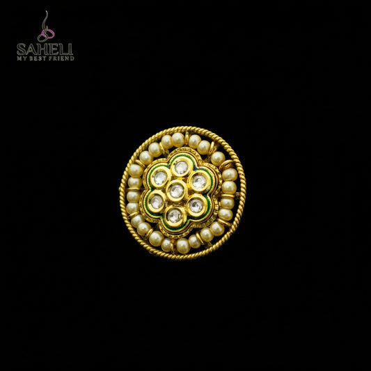 A gold-plated Indian Kundan ring with white pearls and clear stones, displayed on a dark reflective surface. The Saheli My First Jewelry brand logo is visible in the top left corner.