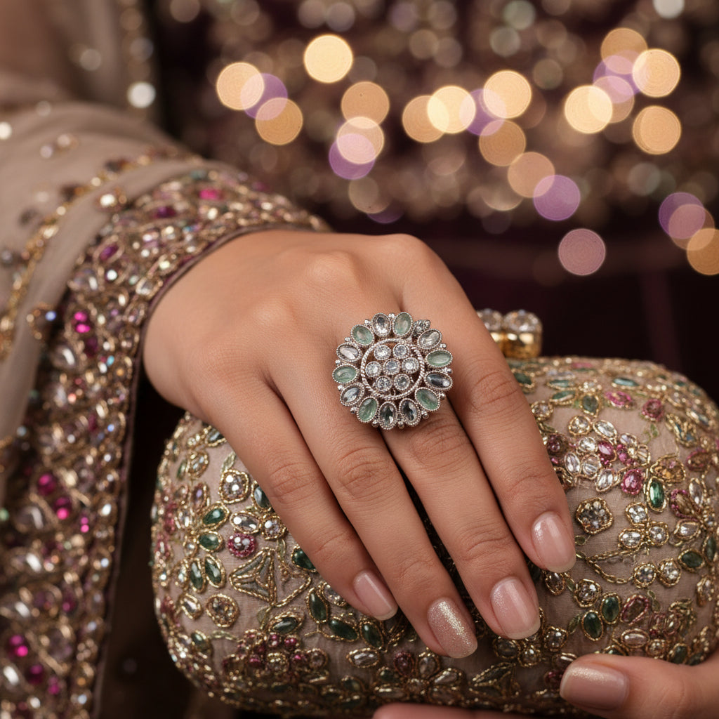 A large, ornate silver-toned ring with multiple oval green stones and small clear center stones, displayed on a black velvet hand. The brand logo 'SAHELI MY BEST FRIEND' is visible above the hand.