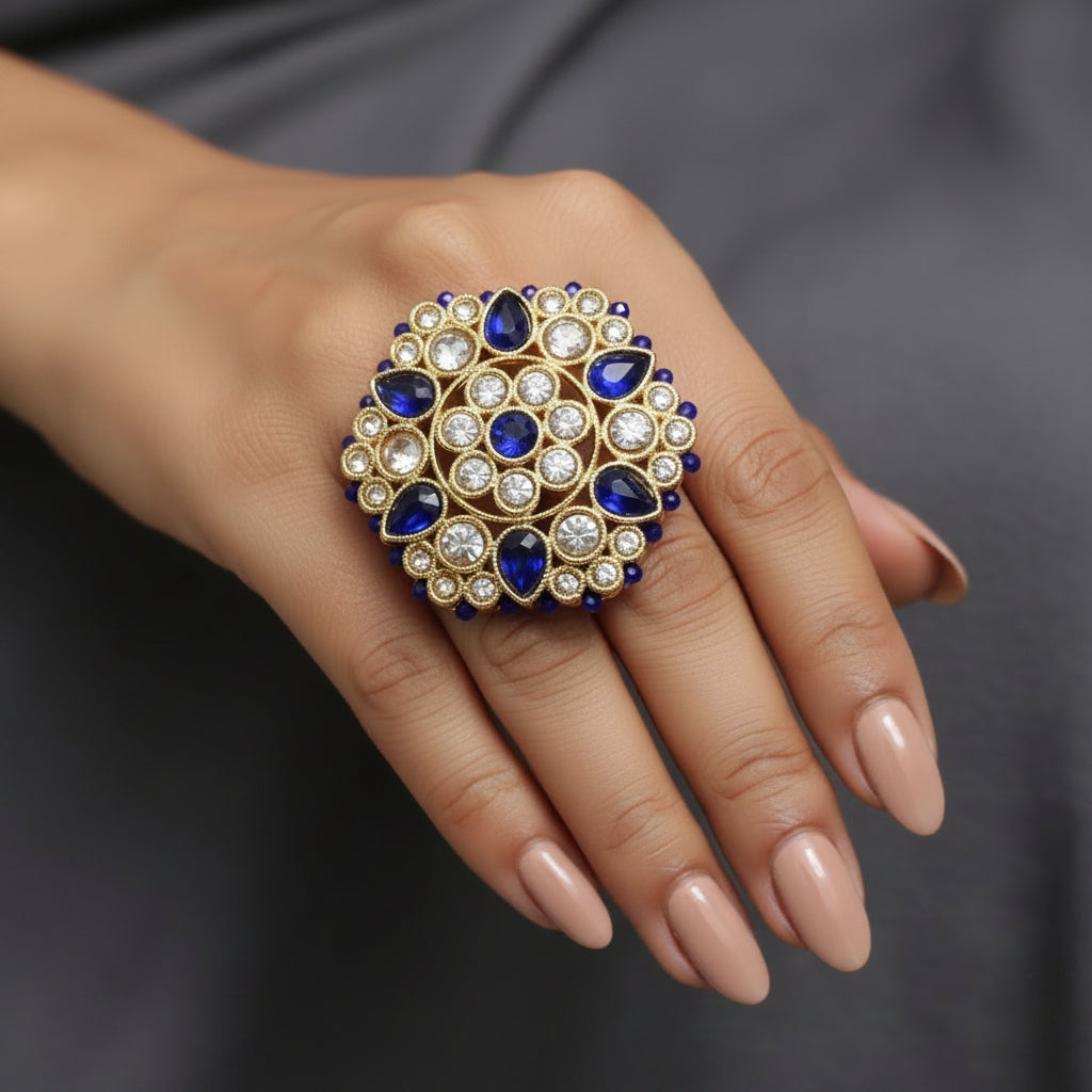 A gold-toned decorative brooch or pin featuring blue teardrop-shaped stones and small clear rhinestones, displayed on a black background next to a white price tag.