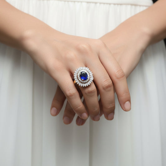 Jewelry ring with blue gemstone and diamond-like stones on a gray background, featuring the brand 'SAHELL'.