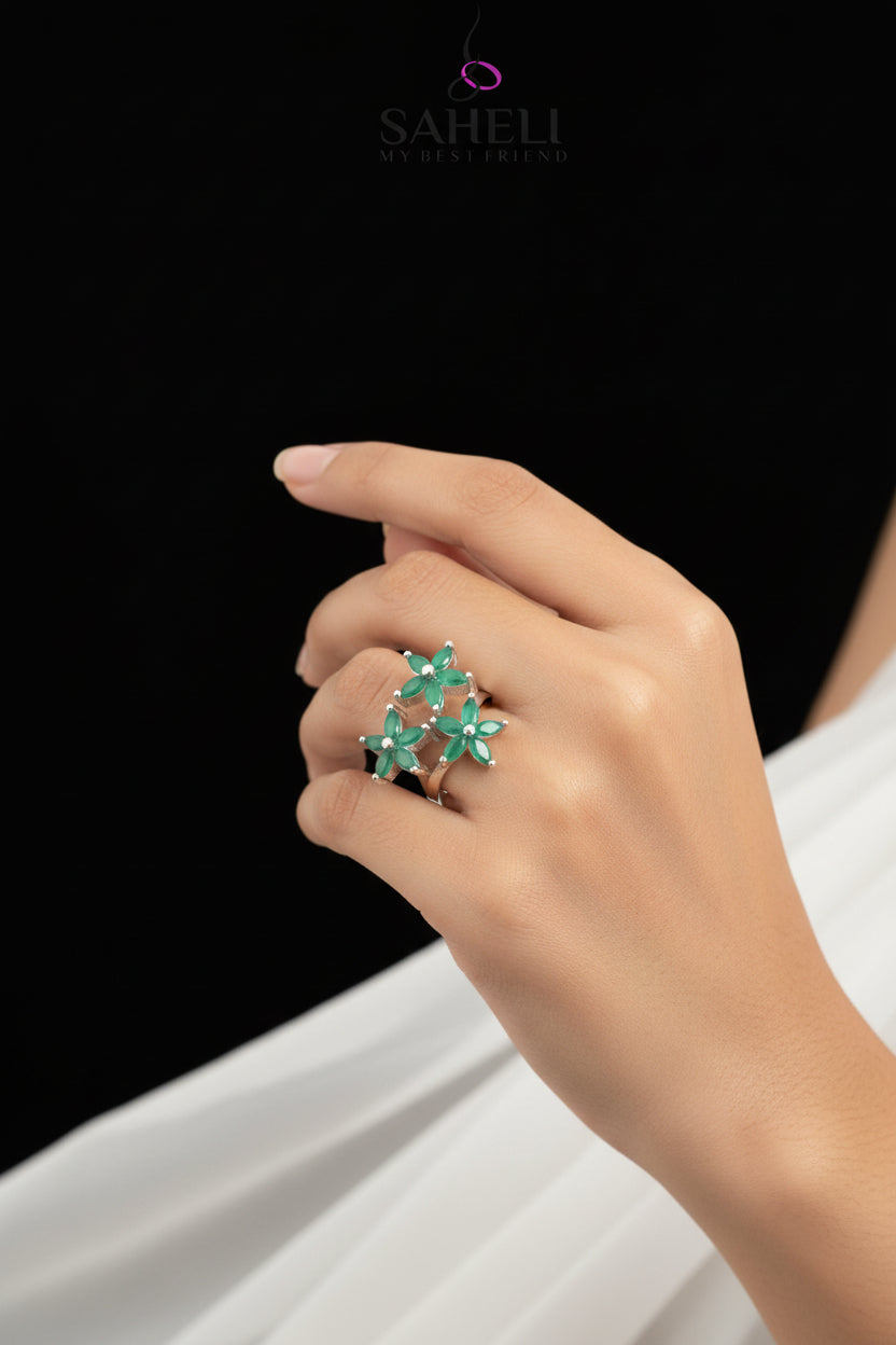 Silver ring with green gemstones on a gray background, featuring the brand 'SAHELI'.
