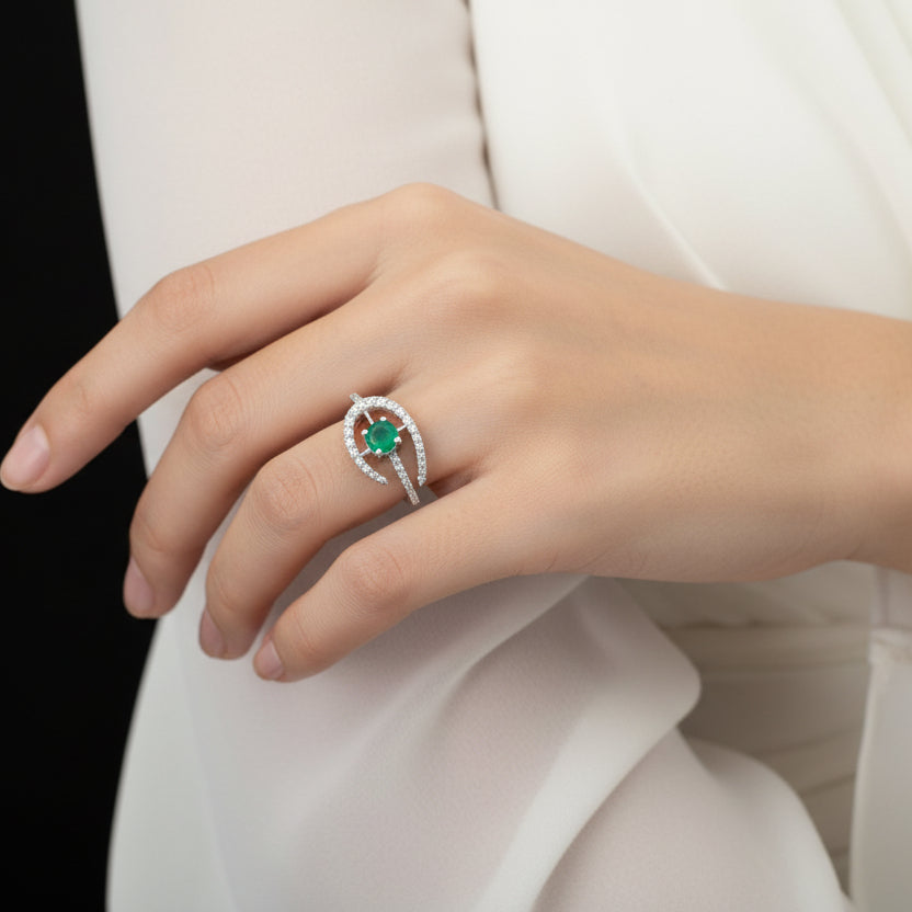 Silver earring with a green gemstone on a black mannequin hand, branded 'Saheli'.