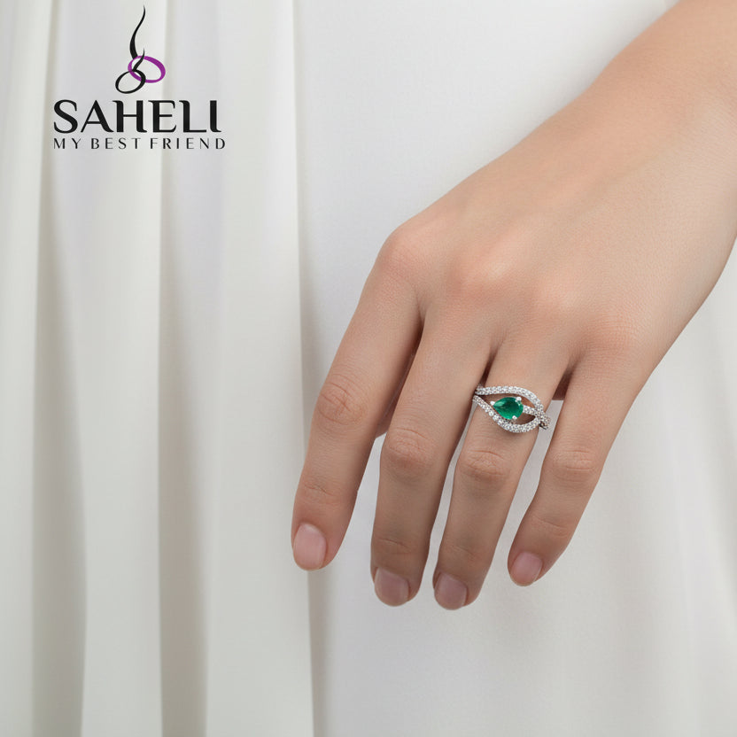 Silver ring with a green gemstone on a black hand, featuring the brand 'SAHELI'.