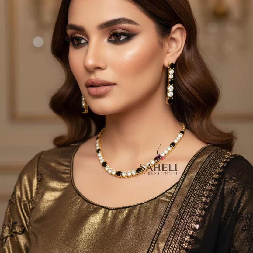Gold necklace and earrings with black stones on a dark background, featuring the brand 'Saheli'.