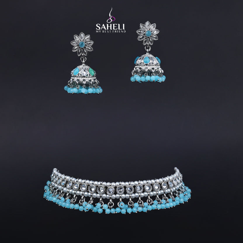 Jewelry set with earrings and a necklace on a black stand, featuring the brand 'Saheli'.