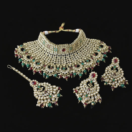 Ornate gold necklace set with green and red stones on a dark background, featuring the brand 'Saheli'.