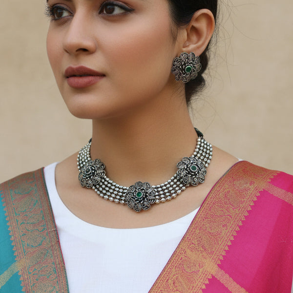 Silver necklace with floral designs and green stones on a dark background