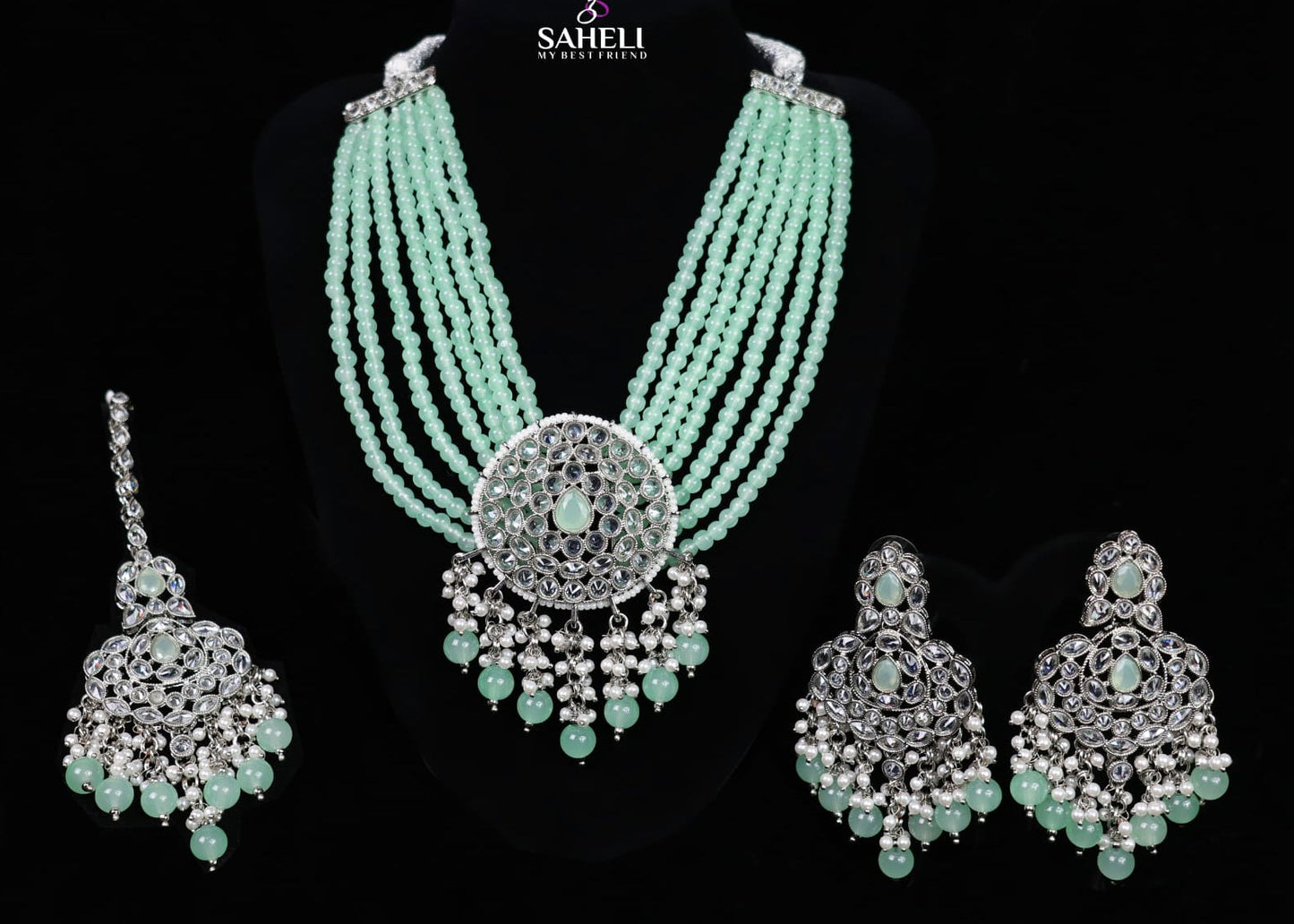 Jewelry set with necklace, earrings, and pendants on a black background with 'Saheli' branding.