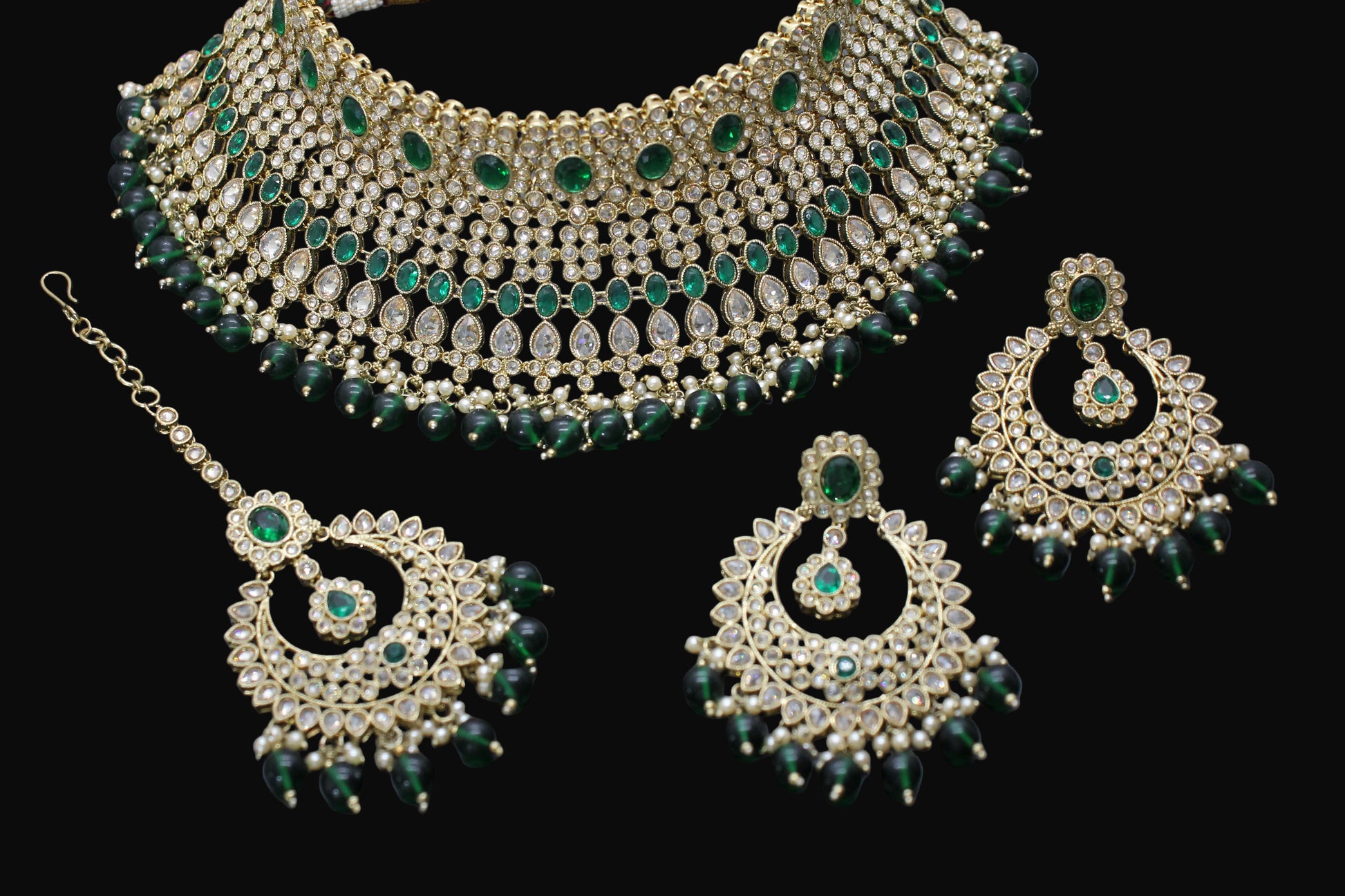 Ornate necklace and earrings with green gemstones on a dark background