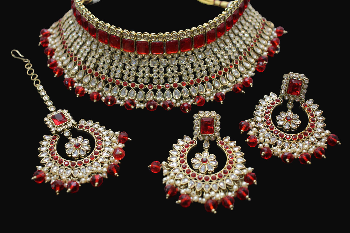 Set of red and gold jewelry including a necklace, earrings, and tikka on a dark background