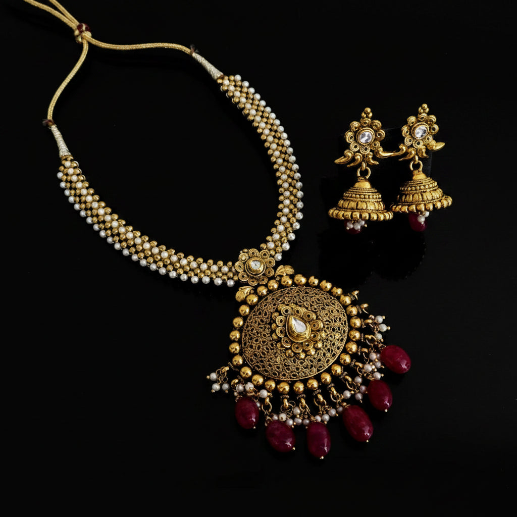Gold necklace with red beads and matching earrings on a black background, branded 'SAHELI'.