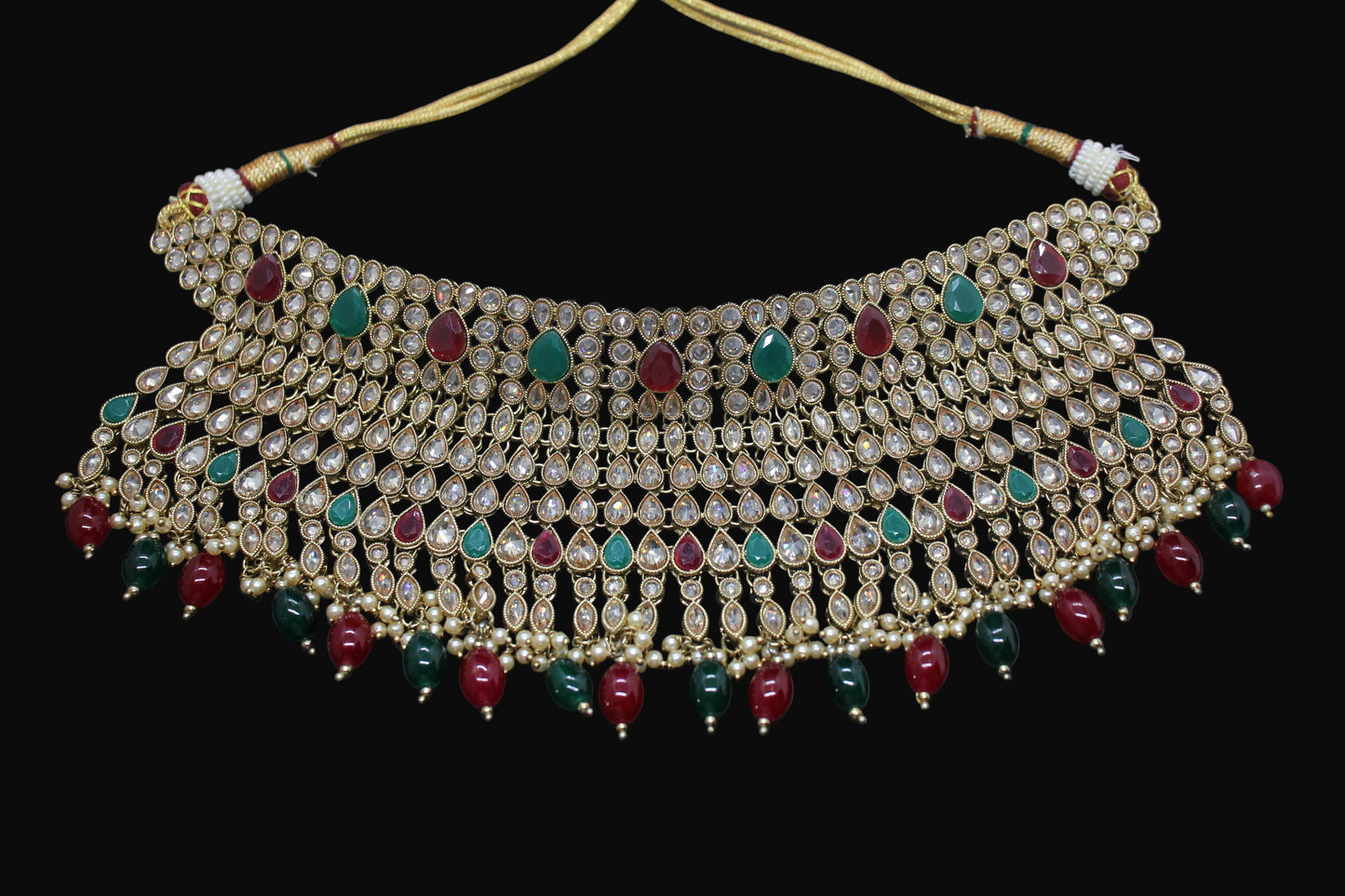 Decorative necklace with pearls, red and green stones on a dark background