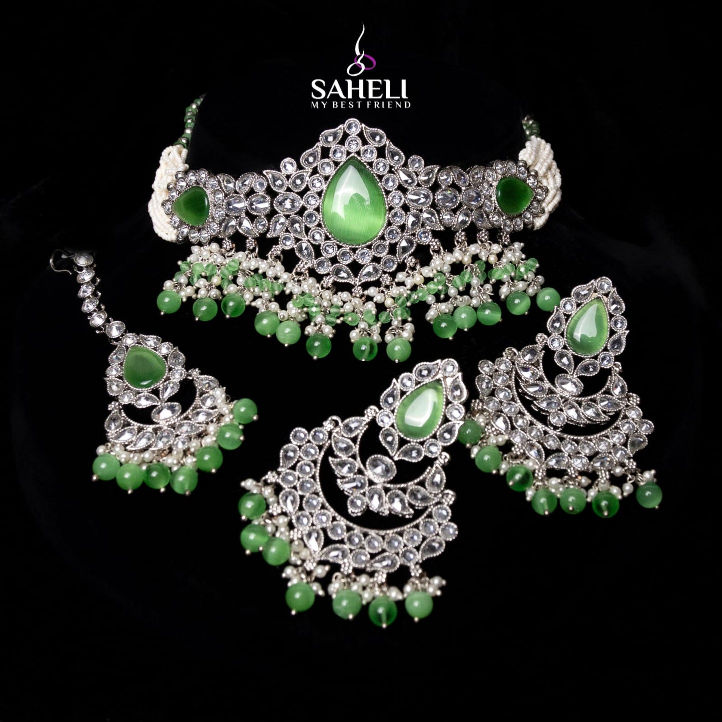 Jewelry set with green stones and silver accents on a black background, featuring the brand 'Saheli'.