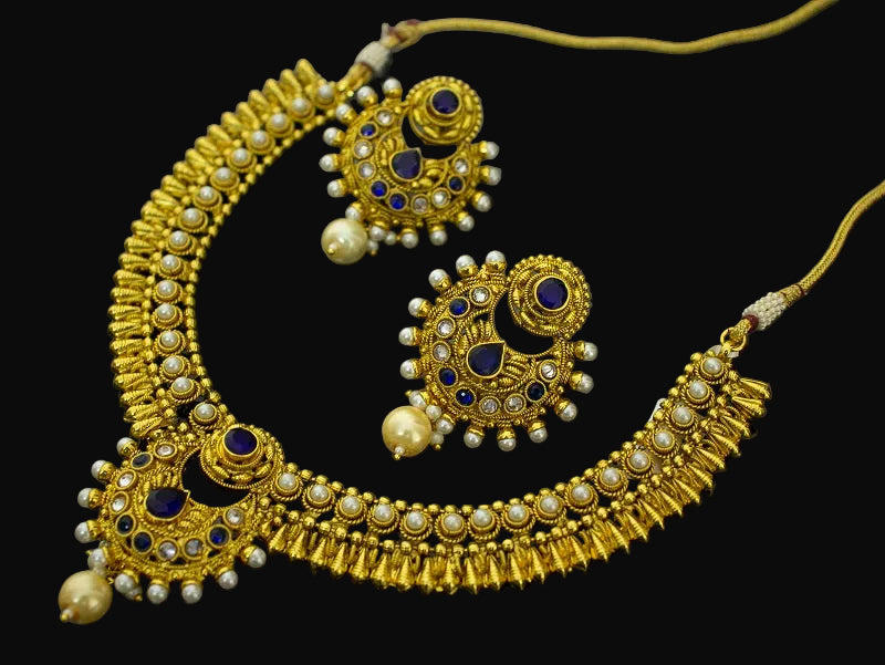 Gold necklace and earrings with blue and pearl accents on a dark background