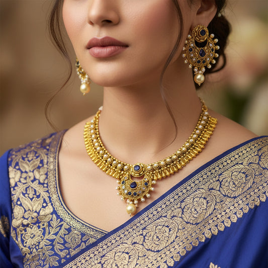 Gold necklace and earrings with blue and pearl accents on a dark background