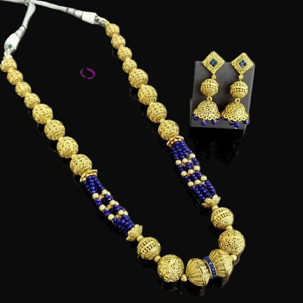 Gold and blue beaded necklace with matching gold earrings displayed on a dark reflective surface. The necklace features textured gold beads, small blue beads, and silver-toned connector details.