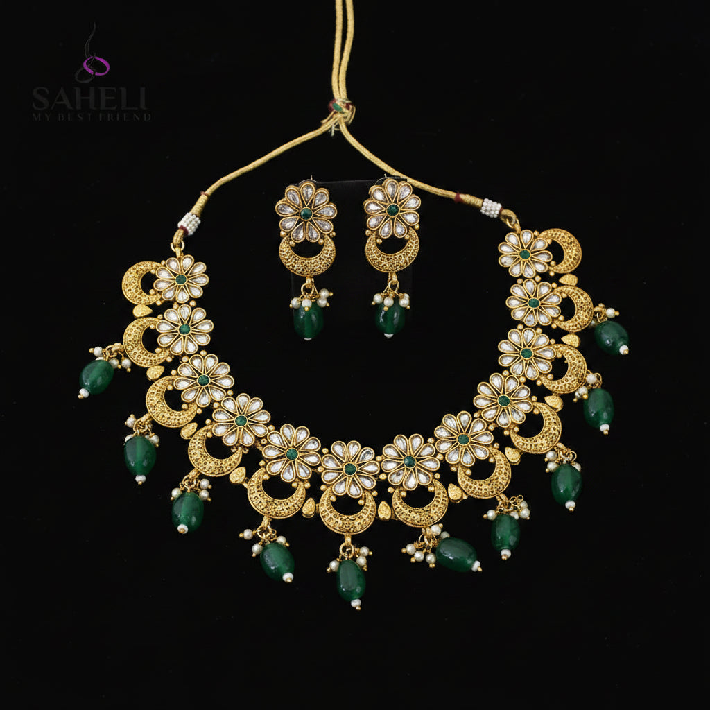 Gold-plated Indian jewelry set featuring a statement necklace and matching earrings with green stone accents and white stones, displayed on a black reflective surface with the SAHELL MY BESTFRIEND logo in the top left corner.