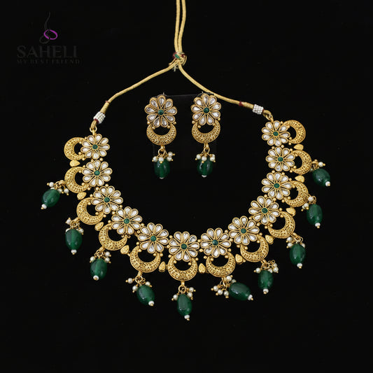Gold-plated Indian jewelry set featuring a statement necklace and matching earrings with green stone accents and white stones, displayed on a black reflective surface with the SAHELL MY BESTFRIEND logo in the top left corner.