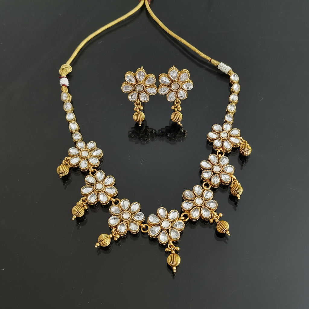 Gold-toned traditional Indian jewelry set featuring a necklace and matching earrings with floral motifs set with clear stones, displayed on a black background. The brand logo 'SAHELI MY BEST FRIEND' is visible in the top right corner.