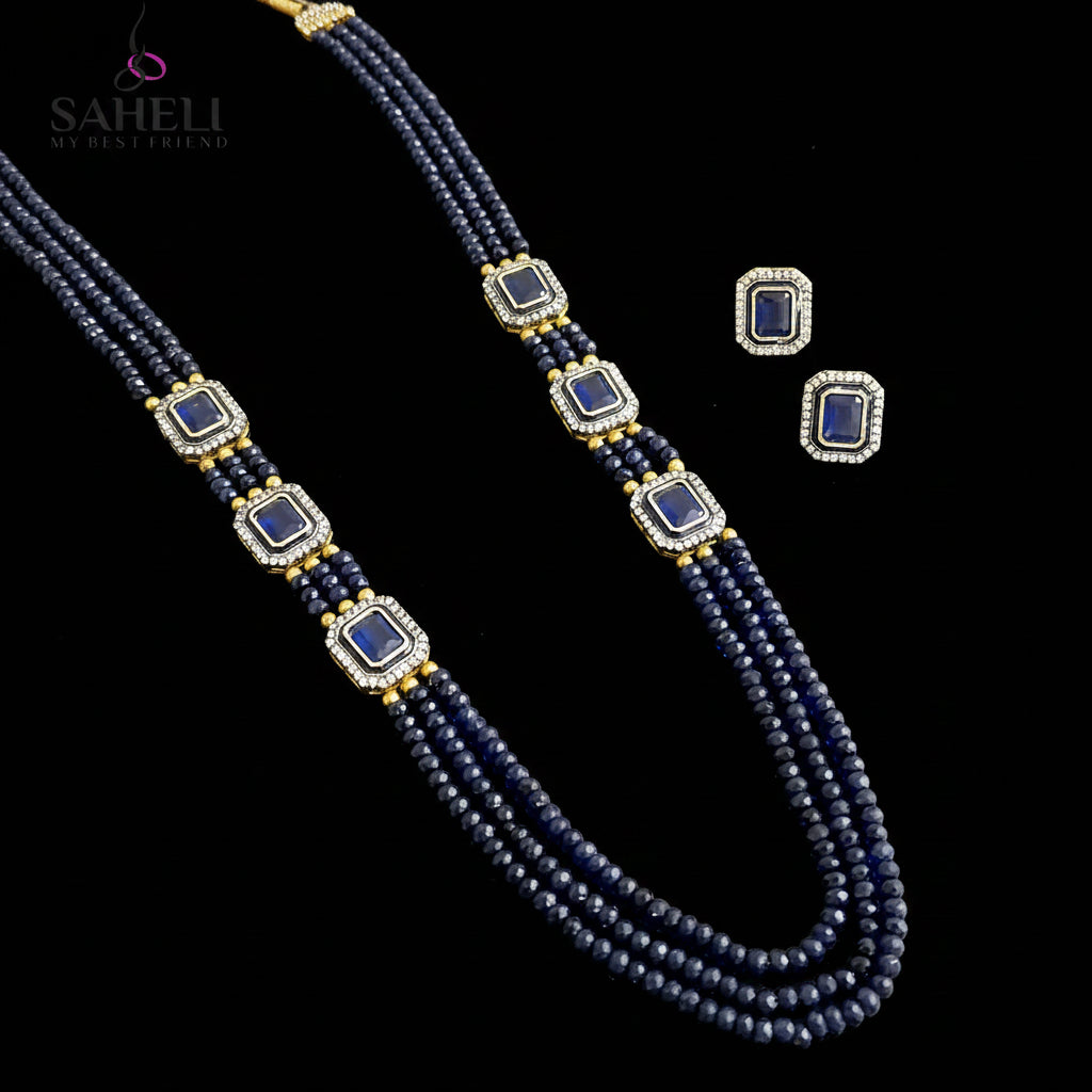 A three-strand beaded necklace and matching stud earrings set by Saheli My Best Friend. The jewelry features dark blue beads, rectangular blue inlays, and gold spacer beads set in silver-tone borders, displayed on a reflective gray surface.