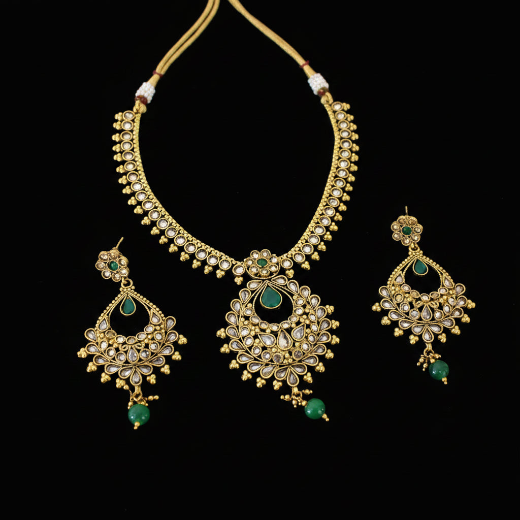 Gold-plated Indian traditional jewelry set including a necklace, earrings, and a central pendant, embellished with white stones and green gemstone accents, displayed on a dark gray background with the brand logo 'SAHeli' visible.
