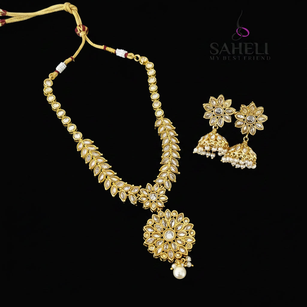 Gold-toned Indian jewelry set featuring a necklace with a large floral pendant, matching flower-shaped earrings, and pearl-like bead accents, displayed on a dark reflective surface with the brand name SAHeli My Best Friend visible in the top right.