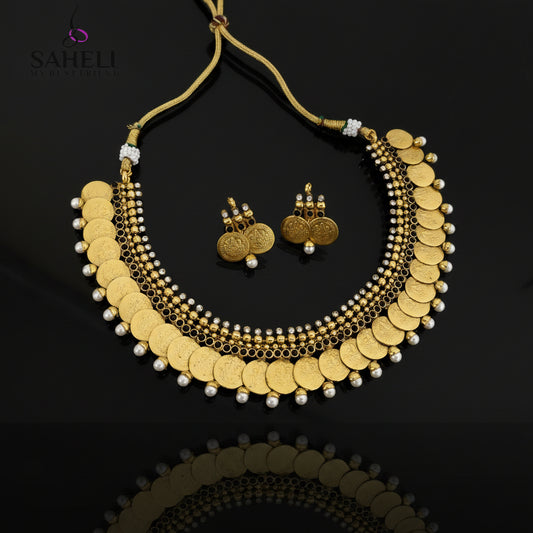 Gold coin necklace and matching gold coin earrings with white pearl accents, displayed on a dark gray reflective surface. The Saheli My Best Friend logo is visible in the top left corner.