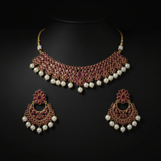 Gold-plated Indian traditional jewelry set featuring a choker necklace and matching earrings, embellished with pinkish-red enamel, white faux pearls, and gold details, displayed on a dark reflective surface.