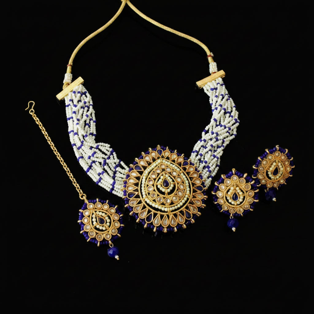 Gold and white beaded Indian jewelry set including a statement necklace, matching earrings, and a maang tikka, displayed on a dark gray background with the Saheli brand logo.