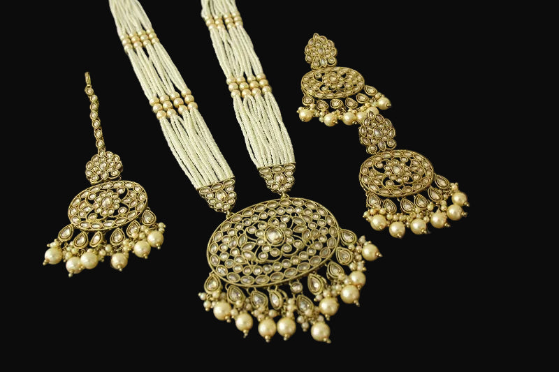 Ornate gold and pearl necklace with matching earrings on a reflective black surface
