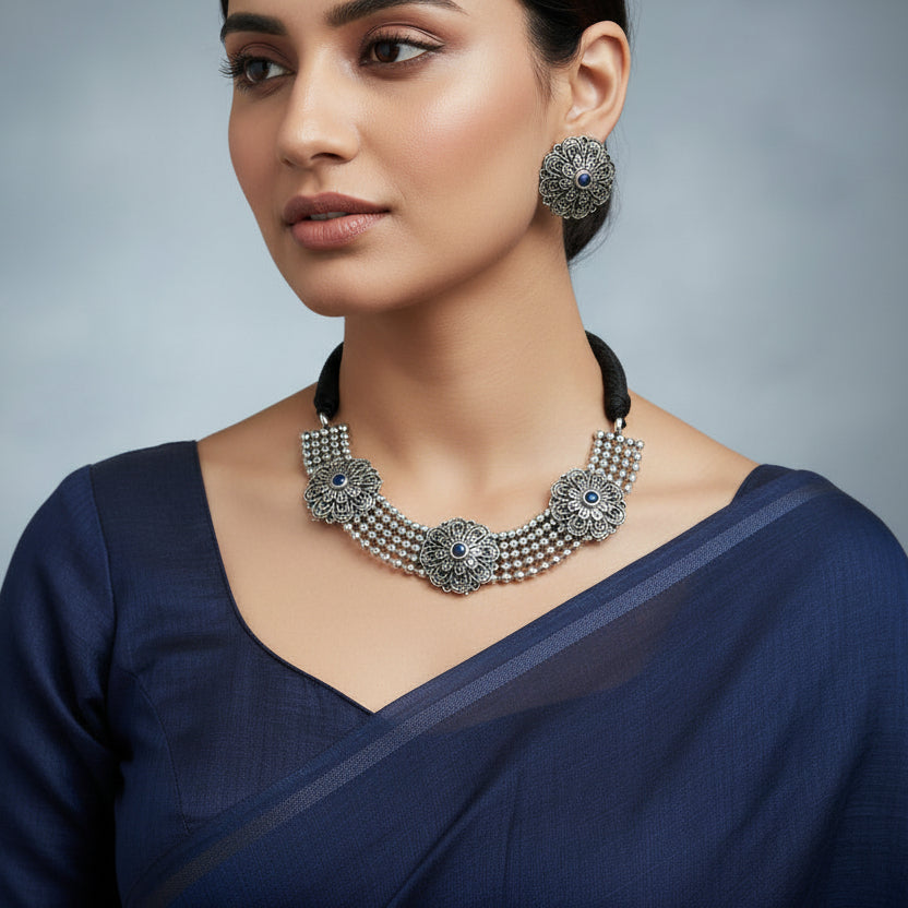 Silver necklace with floral designs and blue stones on a dark background