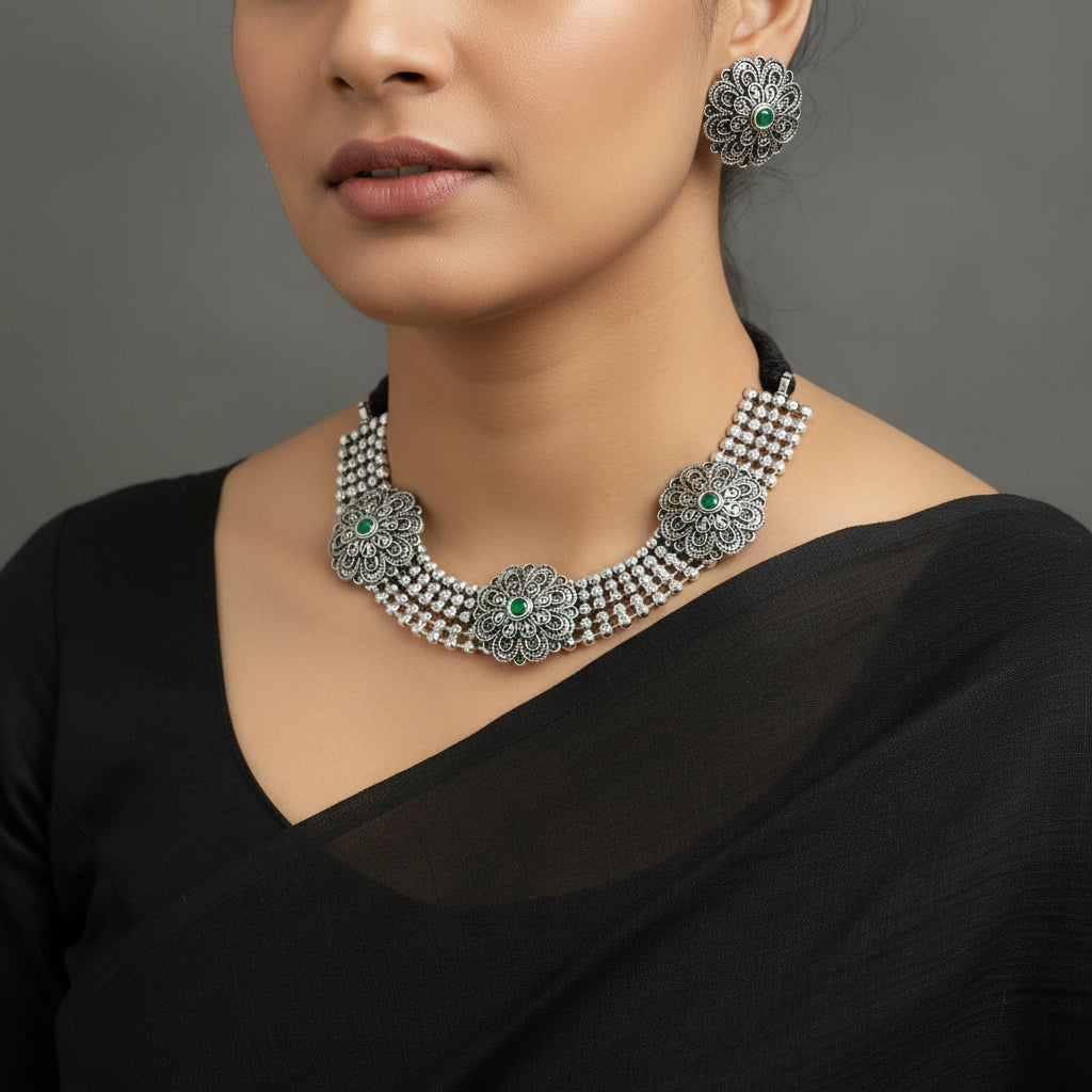 Silver necklace with floral designs and green stones on a reflective surface