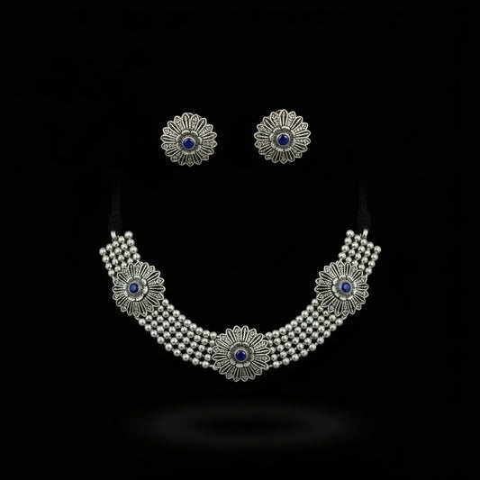 Silver necklace with floral designs and blue stones on a dark background