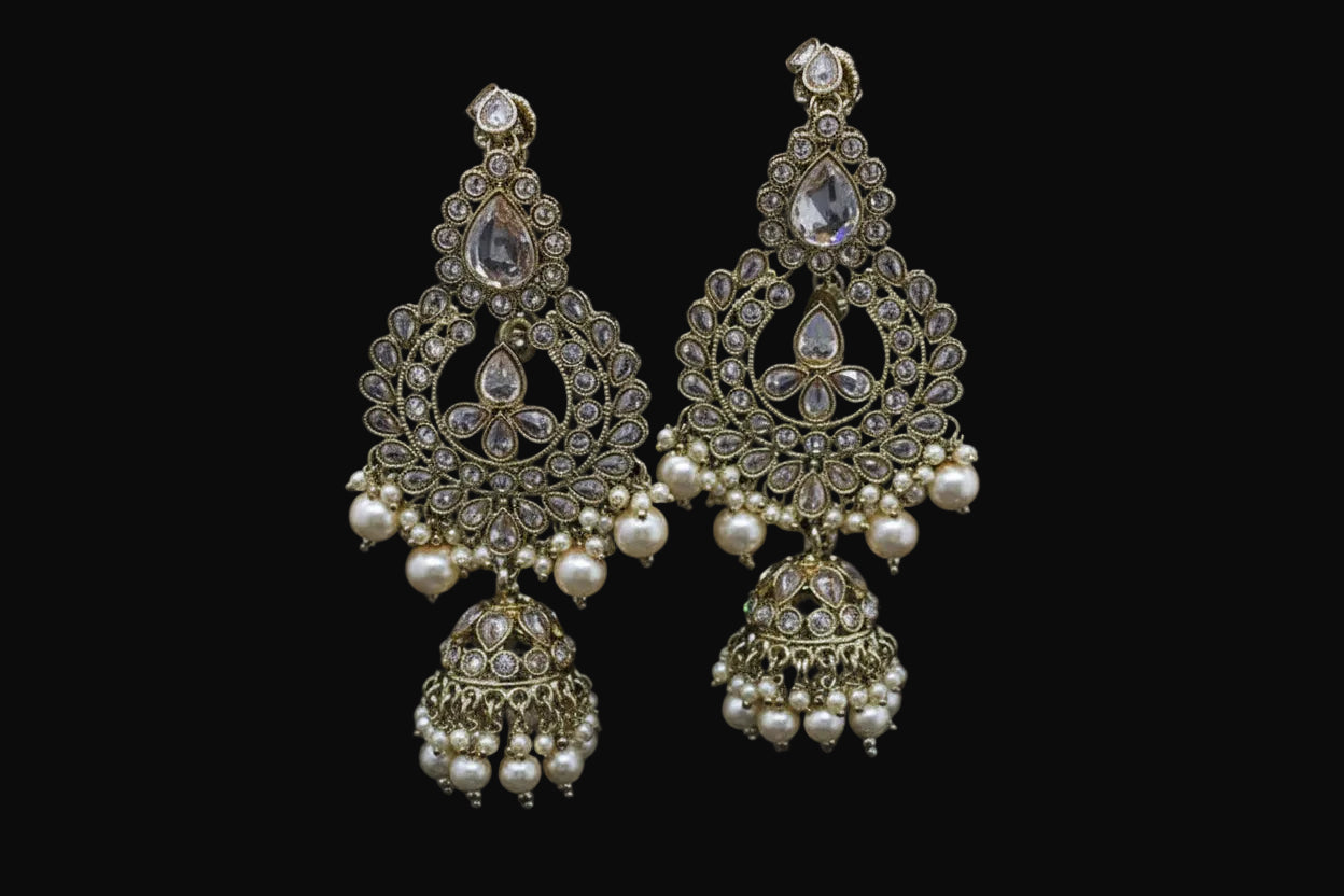 Ornate gold earrings with pearls on a stand, branded 'SAHELI'.