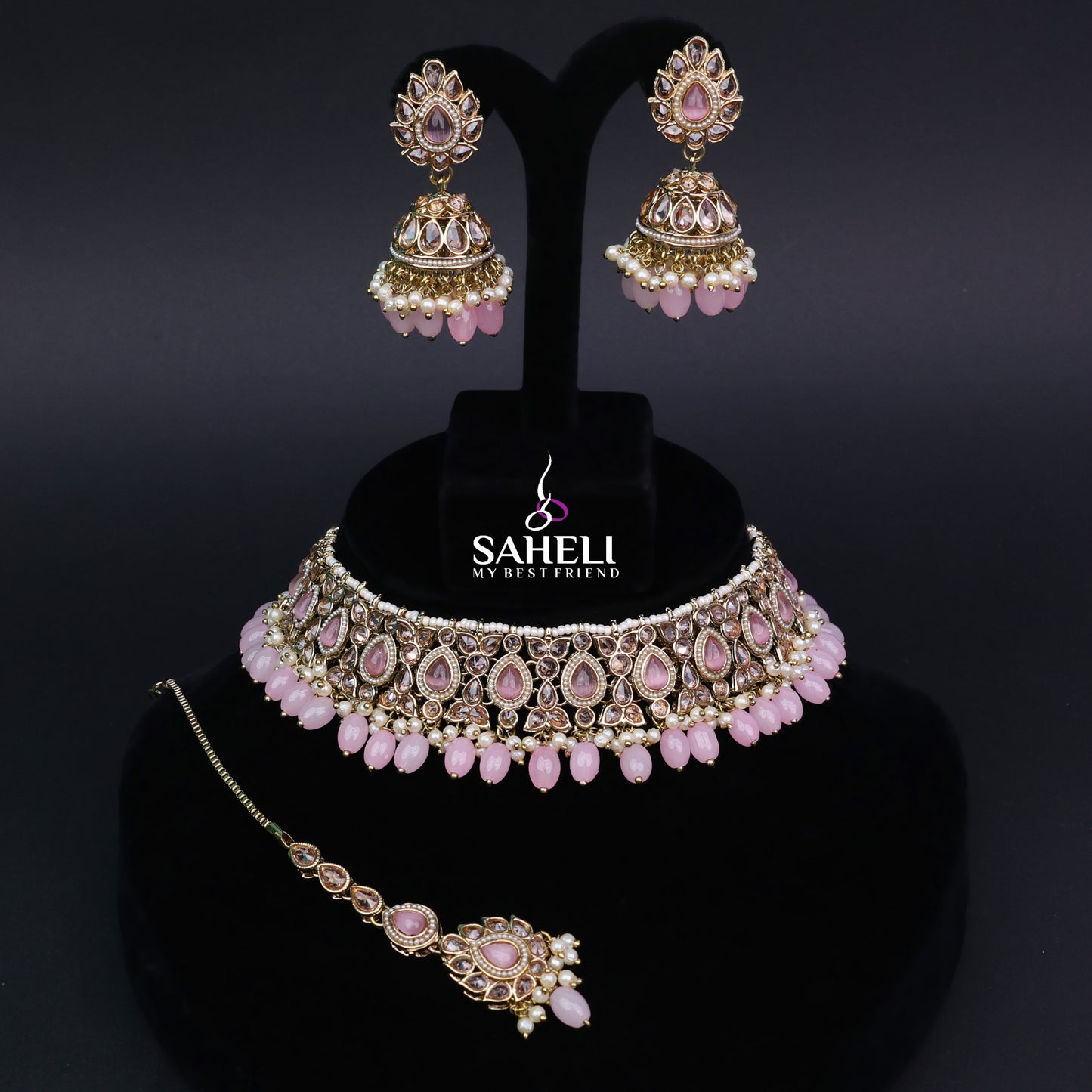 Jewelry set with pink stones on a black stand with 'Saheli' branding.