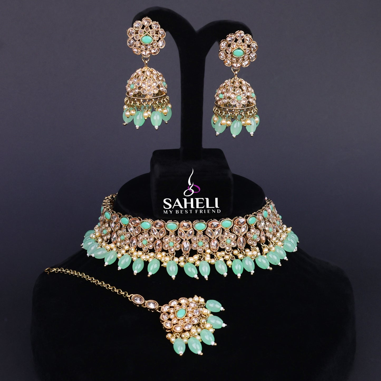Jewelry set with necklace, earrings, and hairpin on a black stand with 'Saheli' branding.