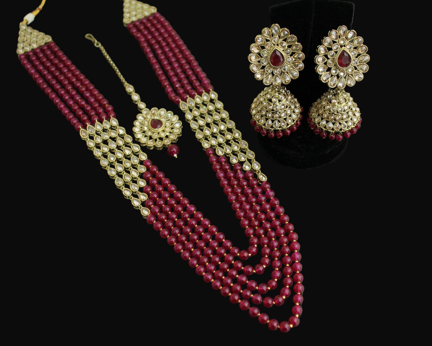 Red beaded necklace with gold accents and matching earrings on a black stand.
